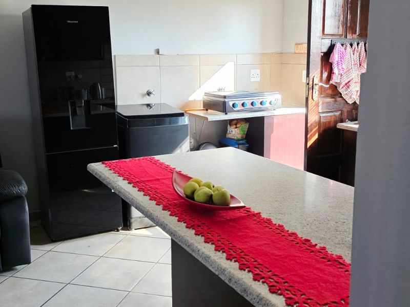A functional kitchen featuring a central island with stone countertop, tiled flooring, and a tiled backsplash, providing a practical workspace.