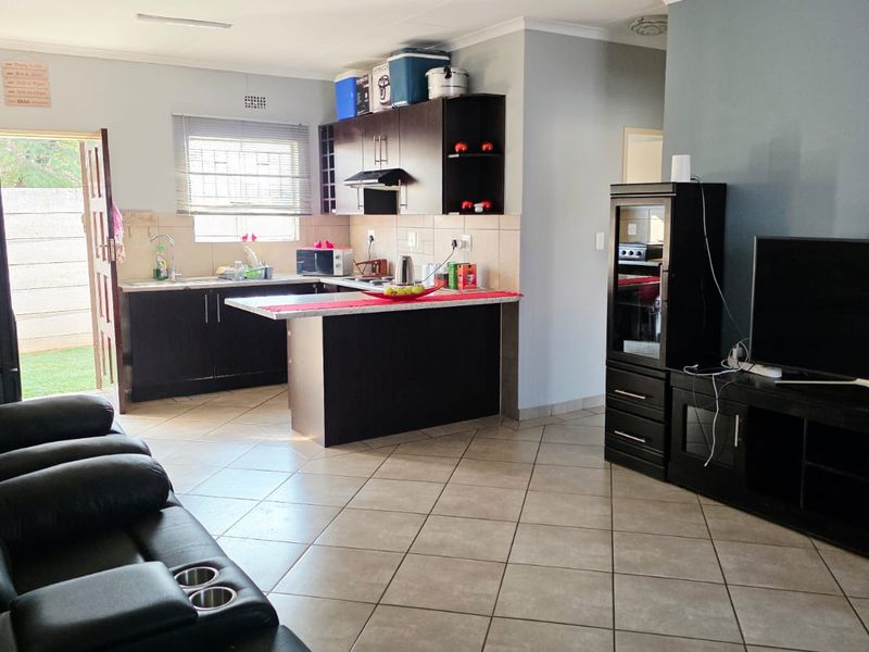 Open-plan living area featuring a kitchen with dark cabinetry, tiled flooring, and a breakfast counter, seamlessly connecting to the lounge space.