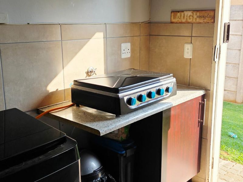 A functional scullery area featuring tiled splashbacks, laminate countertops, built-in cabinetry, and a gas hob, with direct access to the outdoor space.