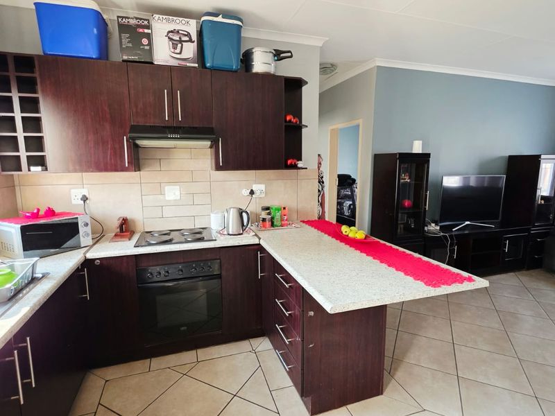 Open-plan kitchen and living area featuring dark wood cabinetry, built-in oven, electric hob, and a functional breakfast bar with tiled flooring throughout.