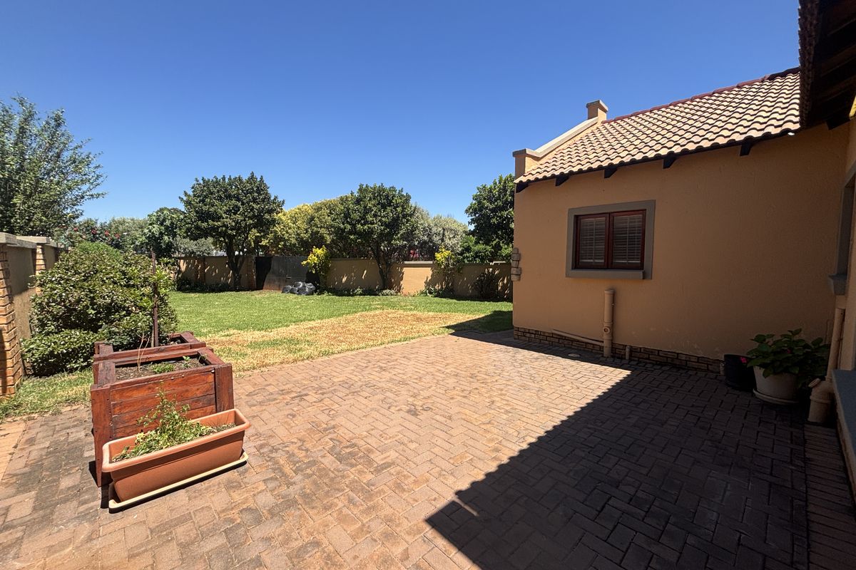 A rear view of the property featuring a paved patio area, a well-maintained lawn, and perimeter walling.