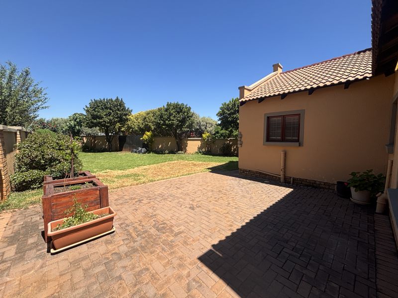 A rear view of the property featuring a paved patio area, a well-maintained lawn, and perimeter walling.