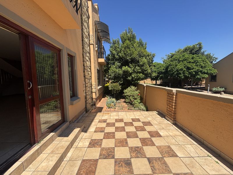 A paved outdoor patio area featuring a checkerboard tile pattern, stone-clad wall accents, and direct access to the interior through a sliding glass door.