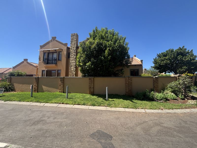 Front elevation of a residential house featuring a stone-clad chimney, tiled roof, and a secure perimeter boundary wall with a paved driveway.