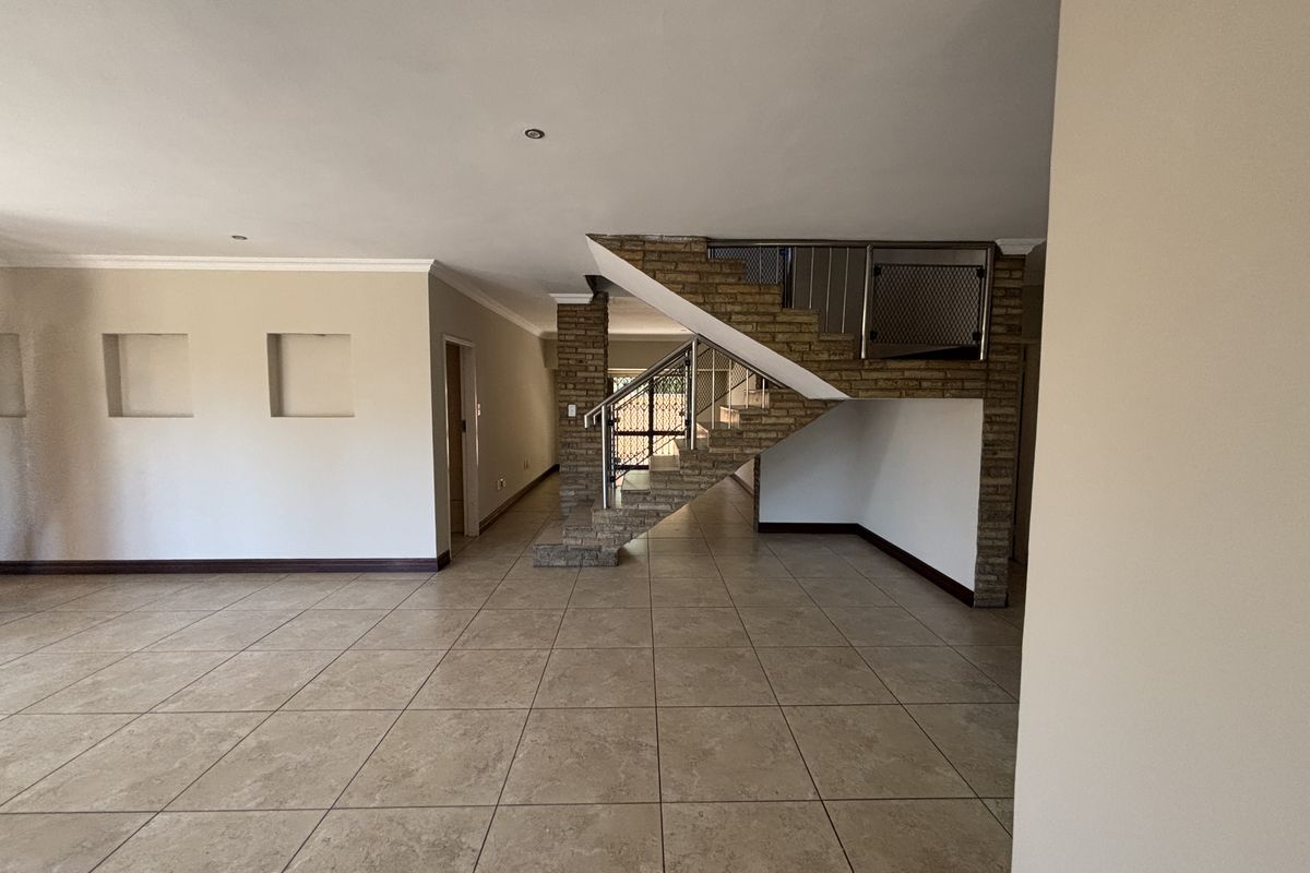 Spacious open-plan living area featuring neutral tiled flooring, a distinctive brick staircase with metal balustrade, and decorative recessed wall niches.