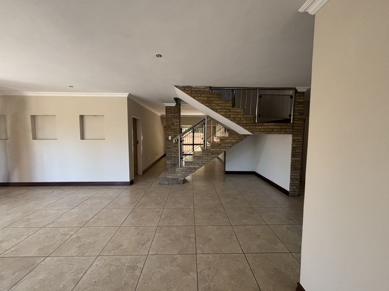 Spacious open-plan living area featuring neutral tiled flooring, a distinctive brick staircase with metal balustrade, and decorative recessed wall niches.