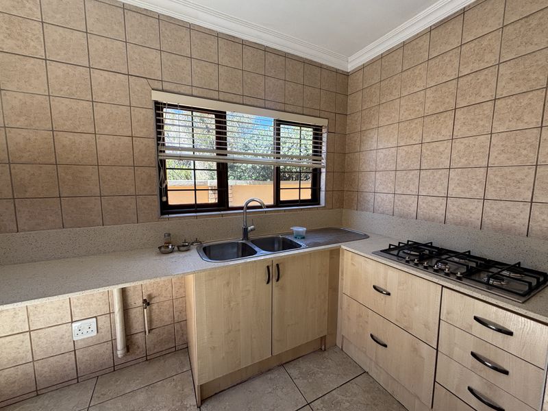 A functional kitchen featuring light wood cabinetry, stone countertops, a double sink, and a built-in gas hob with full-height tiled wall finishes.