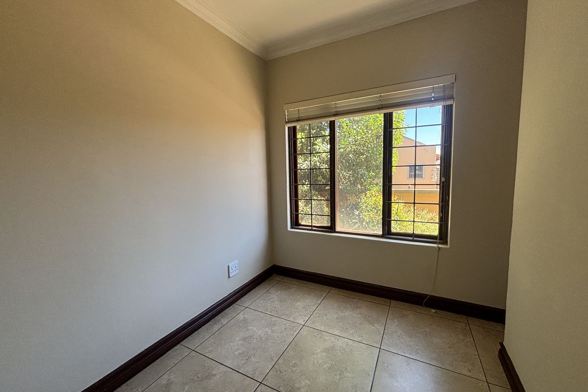 A clean, empty bedroom featuring neutral wall paint, tiled flooring, and a window fitted with security bars.