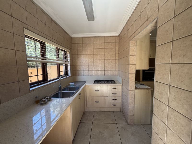 A functional scullery featuring stone countertops, a double sink, gas hob, and ample built-in cabinetry with neutral wall and floor tiling.
