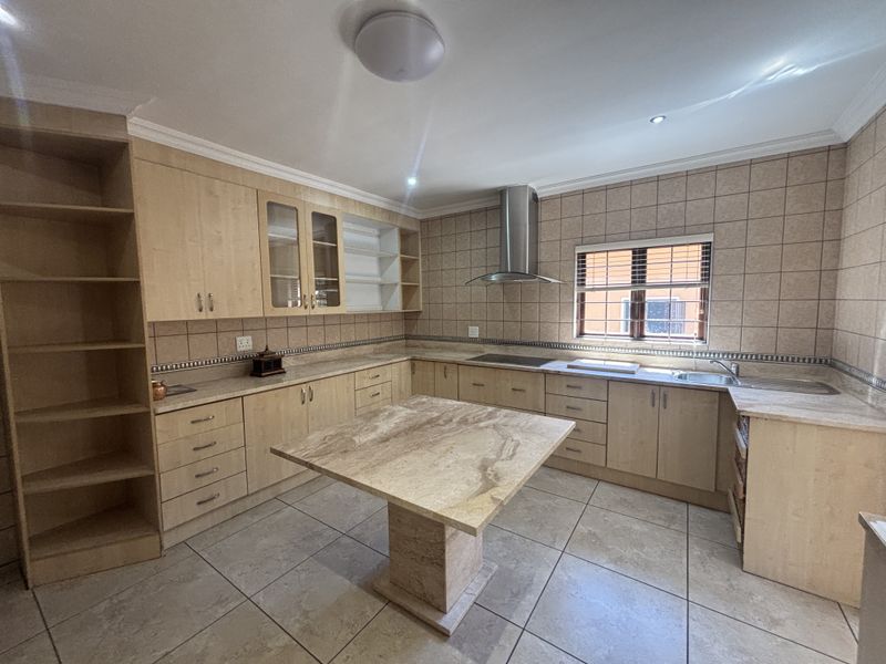Spacious kitchen featuring light wood cabinetry, stone countertops, a central stone island, and tiled finishes throughout, offering a functional and well-maintained workspace.