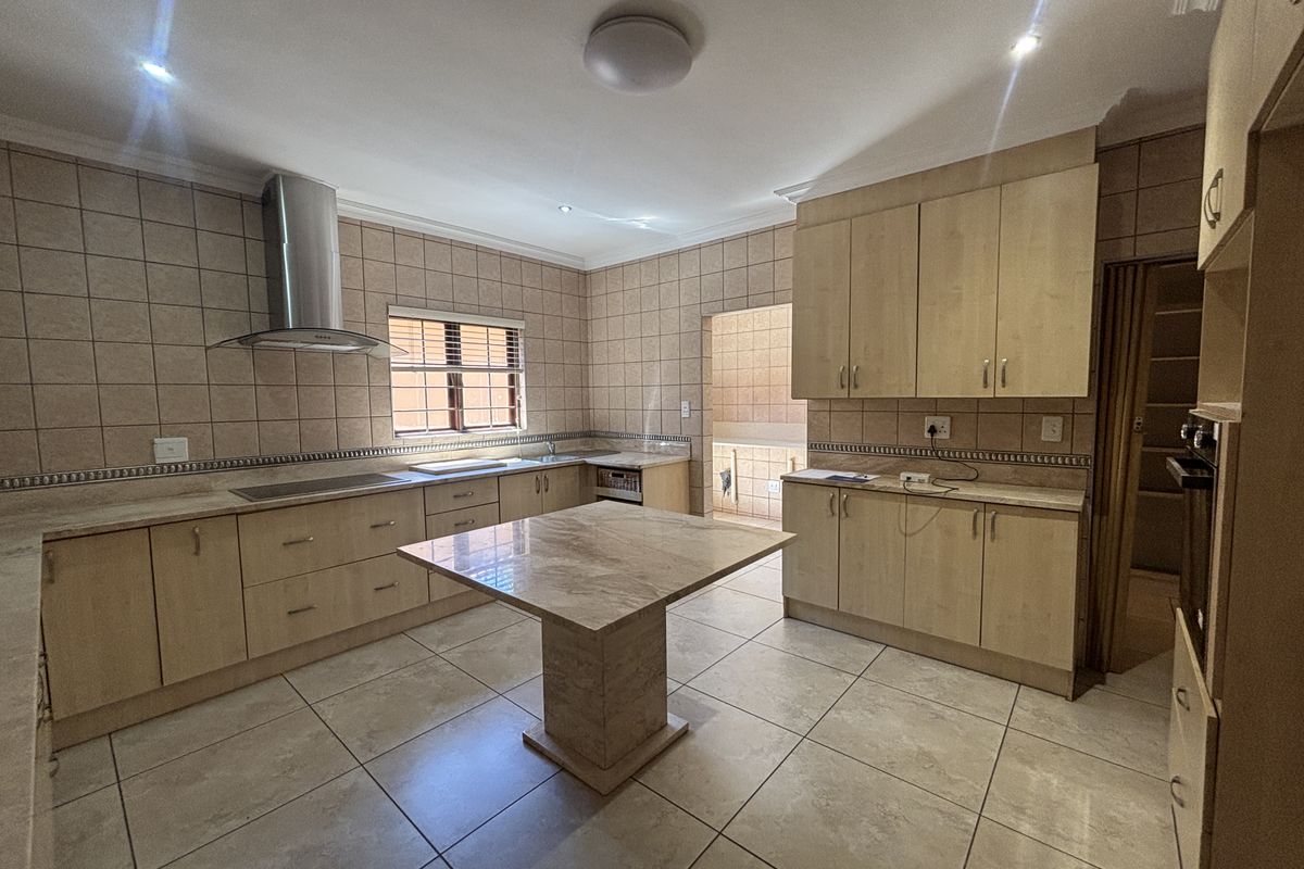 Spacious kitchen featuring light wood cabinetry, stone countertops, a central island, and tiled finishes throughout, offering a functional layout with ample storage space.