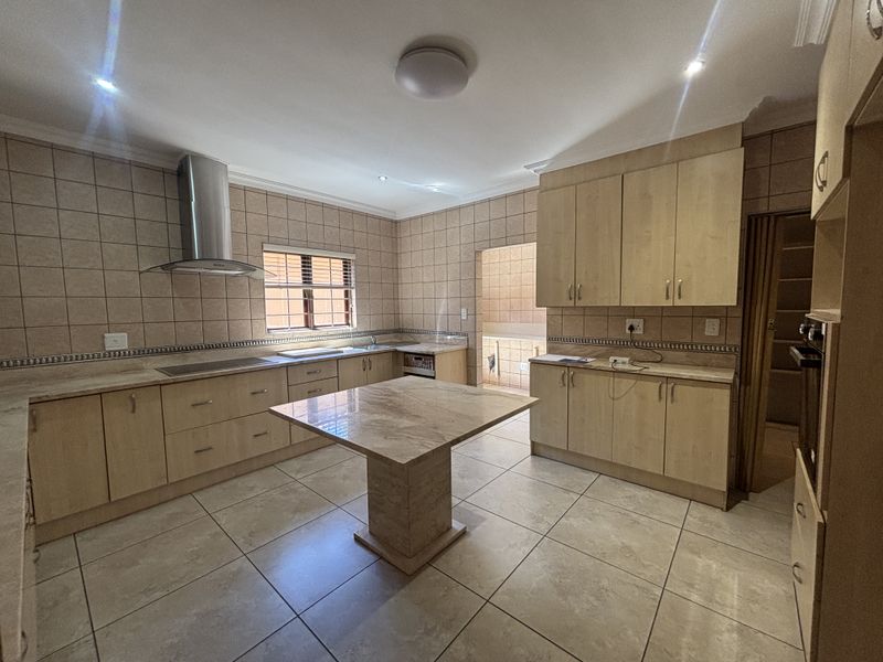 Spacious kitchen featuring light wood cabinetry, stone countertops, a central island, and tiled finishes throughout, offering a functional layout with ample storage space.