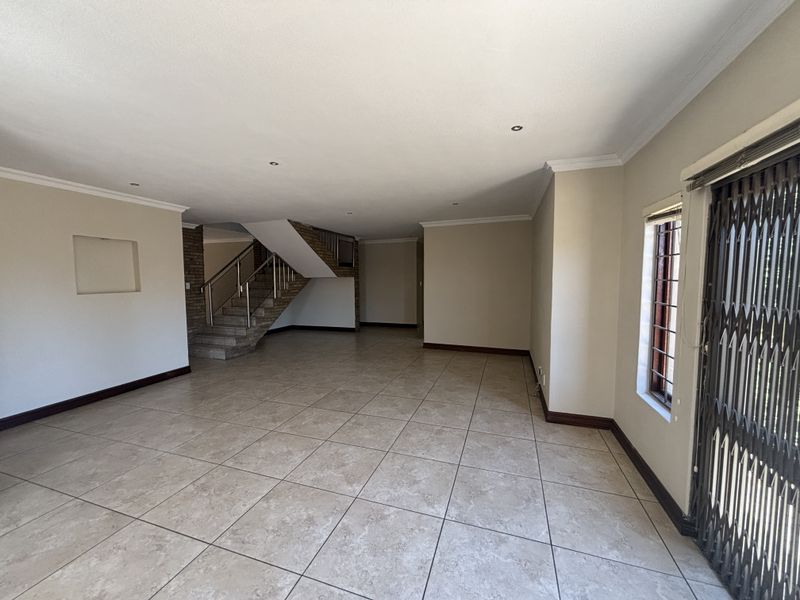 Spacious, open-plan living area featuring neutral tiled flooring, a central staircase with stainless steel balustrades, and recessed lighting throughout.