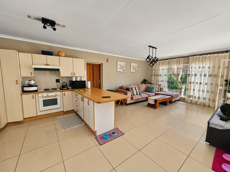 Spacious open-plan living area featuring a functional kitchen with built-in cabinetry, oven, and hob, flowing into a bright lounge with large sliding glass doors.