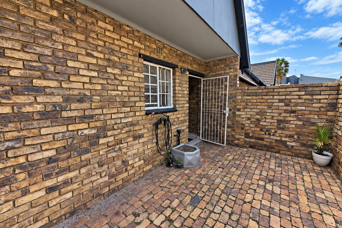 A private rear courtyard featuring face brick walls, paved flooring, and a secure entrance door with a metal security gate.