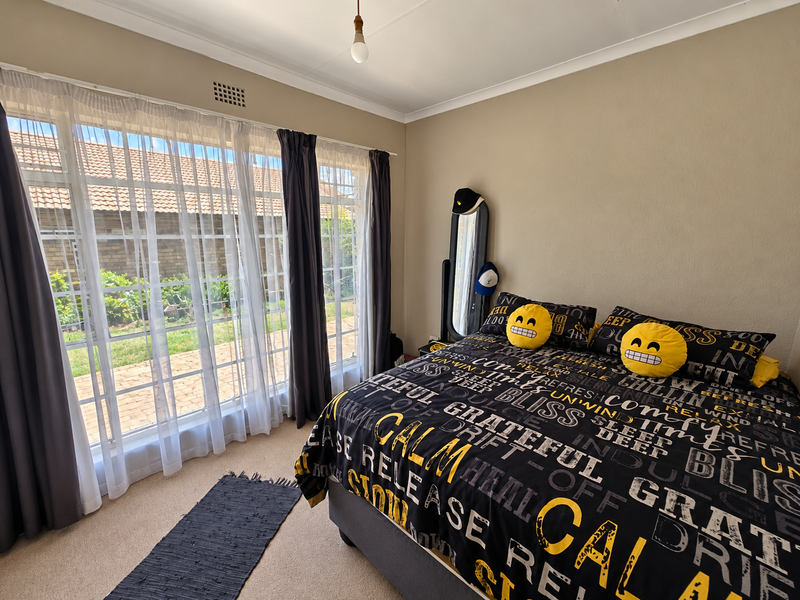 A bright bedroom featuring large windows with garden views, neutral wall tones, and carpeted flooring.