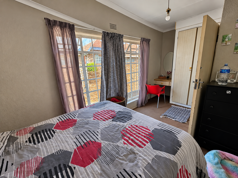 A functional bedroom featuring a built-in wardrobe, coved ceilings, and large windows with security bars, offering a practical layout for a townhouse.