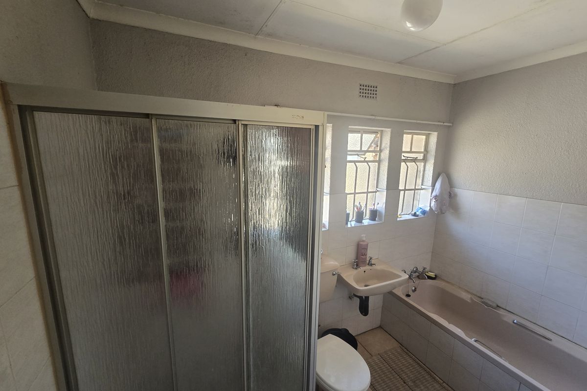 A functional bathroom featuring a shower enclosure, bathtub, wall-mounted basin, and toilet, with security bars on the windows and tiled splashbacks.
