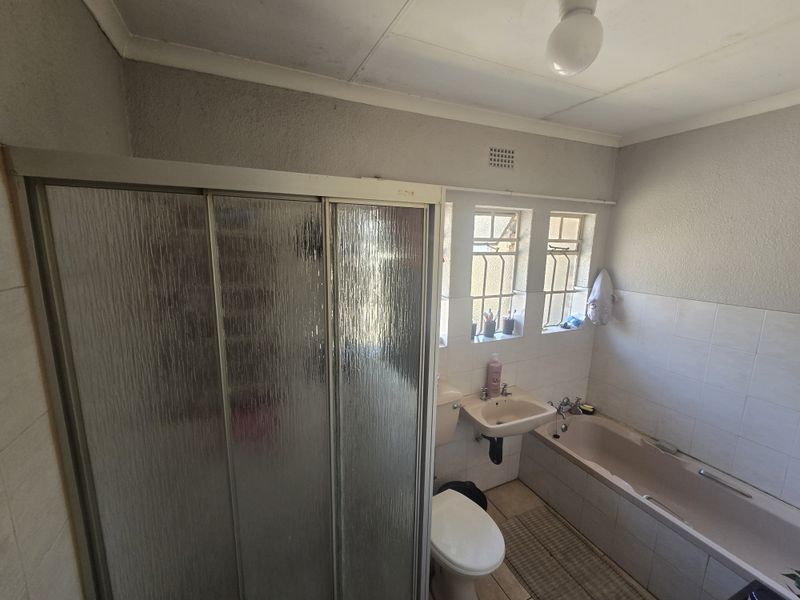 A functional bathroom featuring a shower enclosure, bathtub, wall-mounted basin, and toilet, with security bars on the windows and tiled splashbacks.