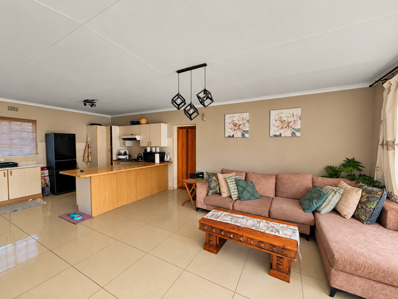 An open-plan living and kitchen area featuring tiled flooring, a breakfast bar, and built-in cabinetry, creating a functional and connected living space.