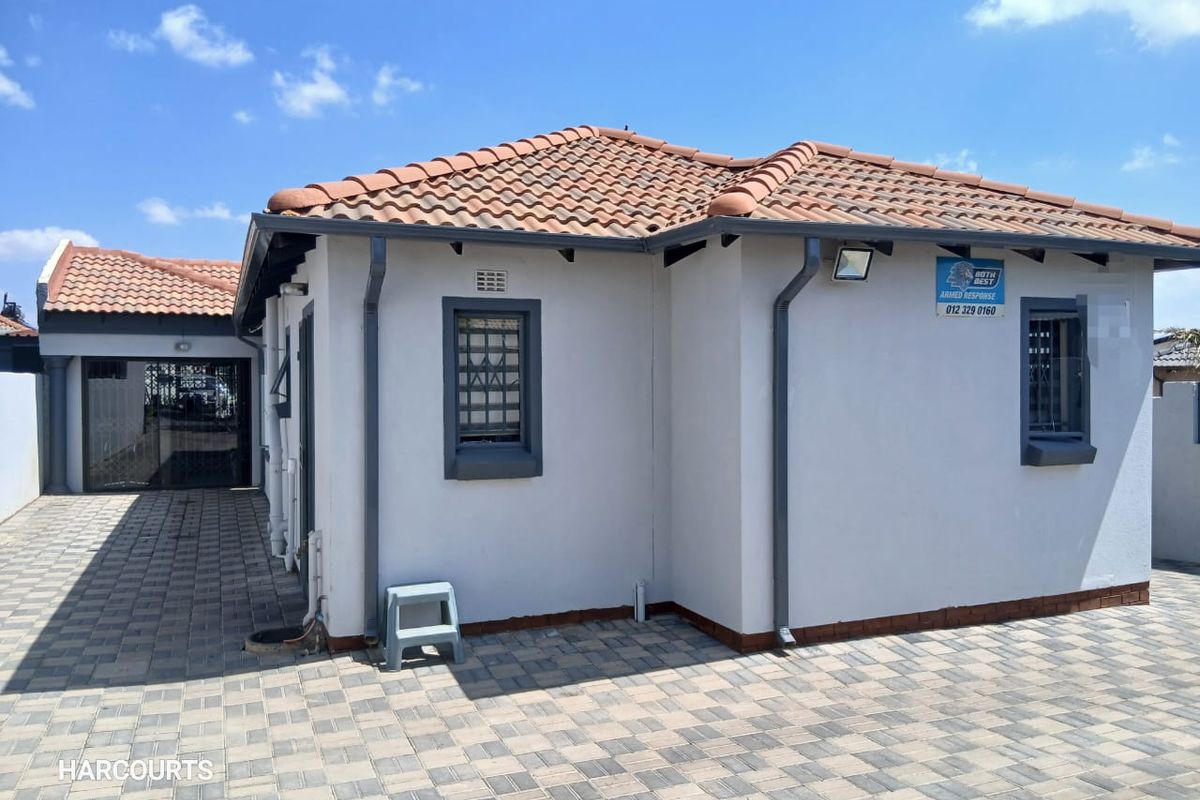 A well-maintained rear exterior view of the house featuring terracotta roof tiles, paved ground surfaces, and secure window fixtures.