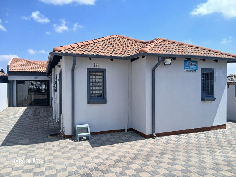 A well-maintained rear exterior view of the house featuring terracotta roof tiles, paved ground surfaces, and secure window fixtures.