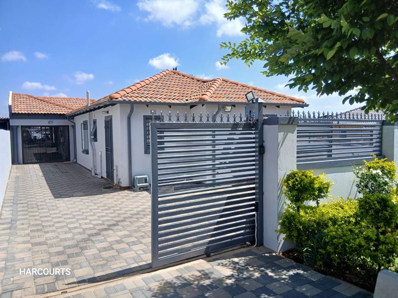 Front exterior view of the property featuring a paved driveway, secure metal sliding gate, perimeter wall with security spikes, and a tiled roof.
