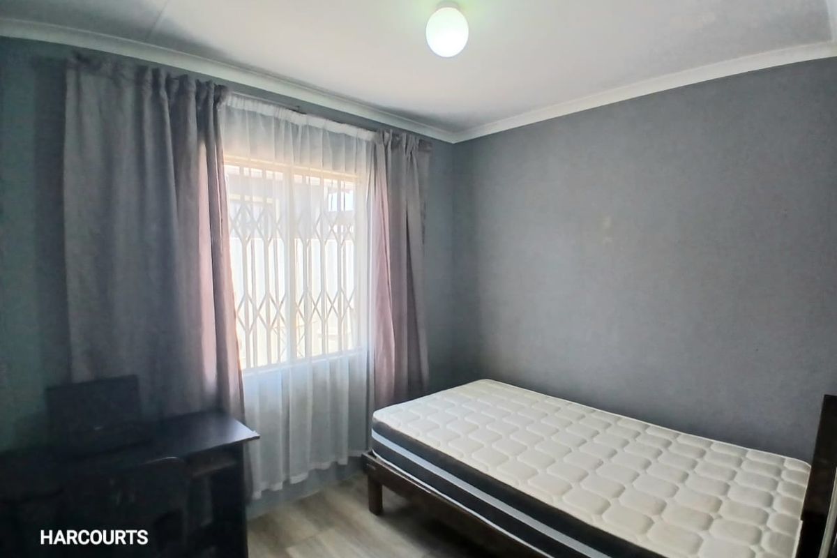 A functional bedroom featuring laminate flooring, neutral grey walls, and a window fitted with a security gate.
