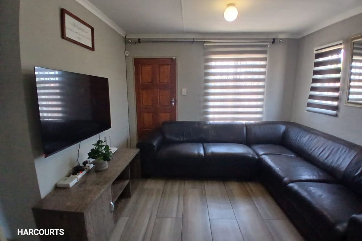 A comfortable living room featuring tiled flooring, modern roller blinds, and a solid timber door, providing a functional and well-maintained space.