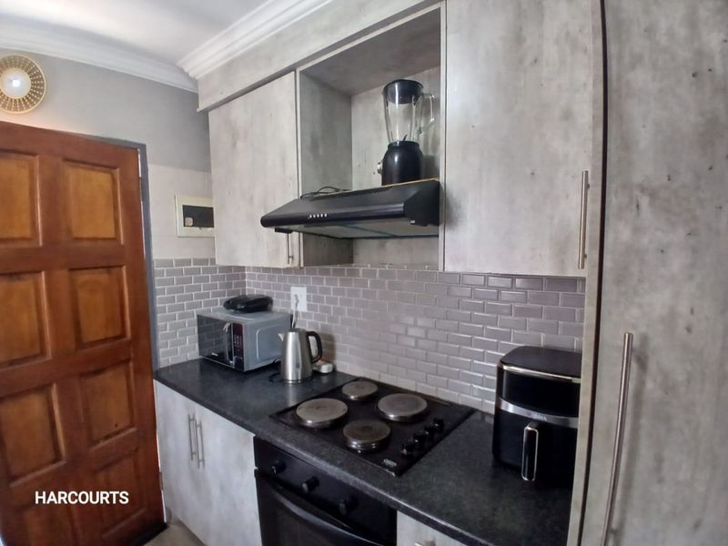 A functional kitchen featuring modern grey cabinetry, subway tile backsplash, stone countertops, and integrated cooking appliances including an electric hob and oven.