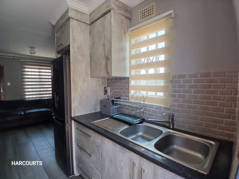 A compact kitchen featuring modern grey-toned cabinetry, subway tile backsplash, and a double bowl stainless steel sink with a view into the adjacent living area.