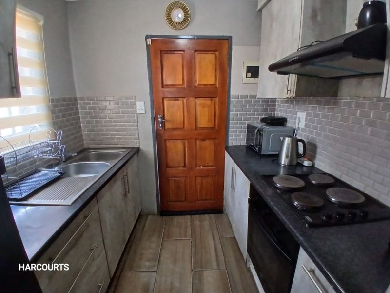 A functional galley-style kitchen featuring subway tile backsplashes, dark countertops, built-in oven, electric hob, and modern cabinetry with tiled flooring.