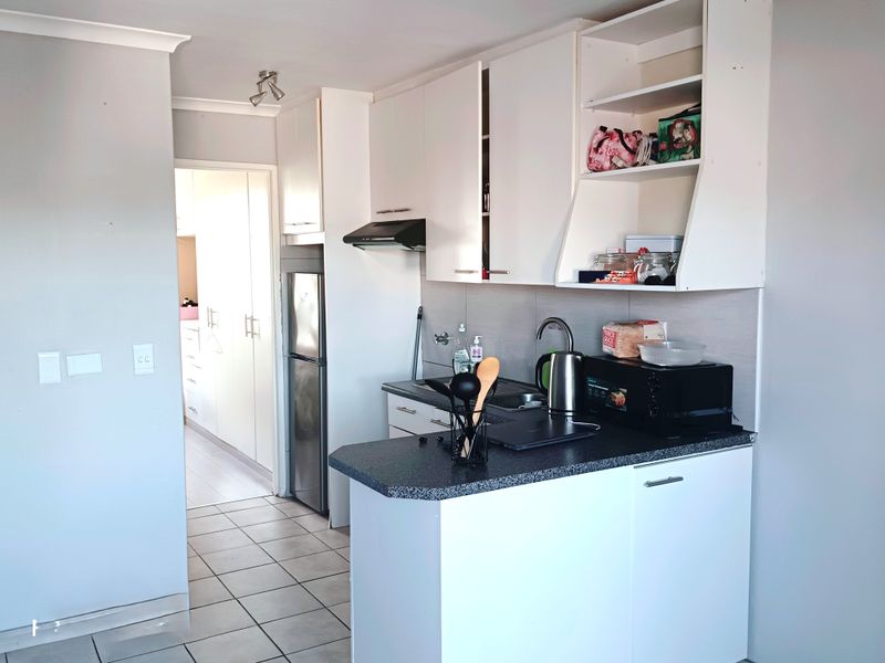 Compact kitchen featuring white built-in cabinetry, dark laminate countertops, a stainless steel sink, and tiled flooring, offering a functional and clean workspace.