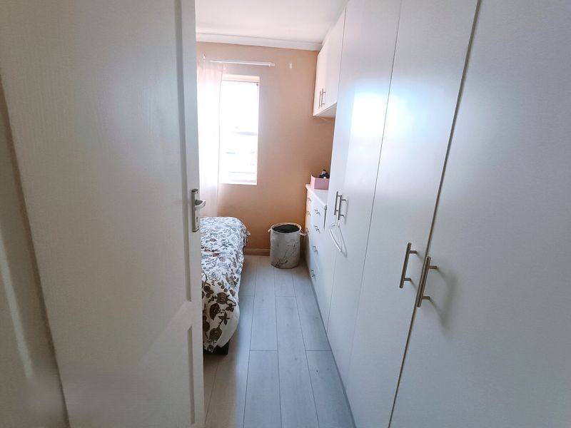 A compact bedroom featuring light-toned laminate flooring and extensive built-in cupboard storage, providing a clean and functional living space.