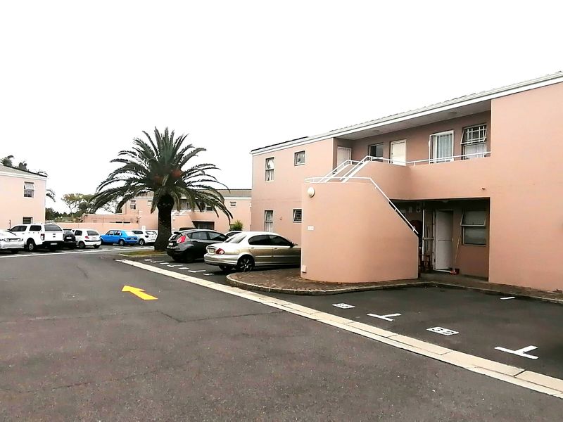 Exterior view of an apartment complex featuring paved parking areas, external staircases, and painted masonry facades.