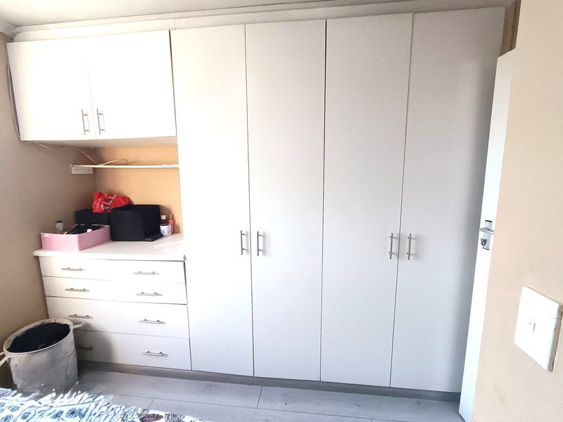 A bedroom featuring white built-in cupboards and a matching vanity unit with drawers, providing ample storage space.