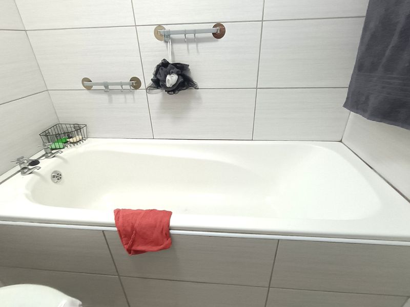 A clean bathroom featuring a built-in bathtub with modern wall tiling and chrome fixtures.