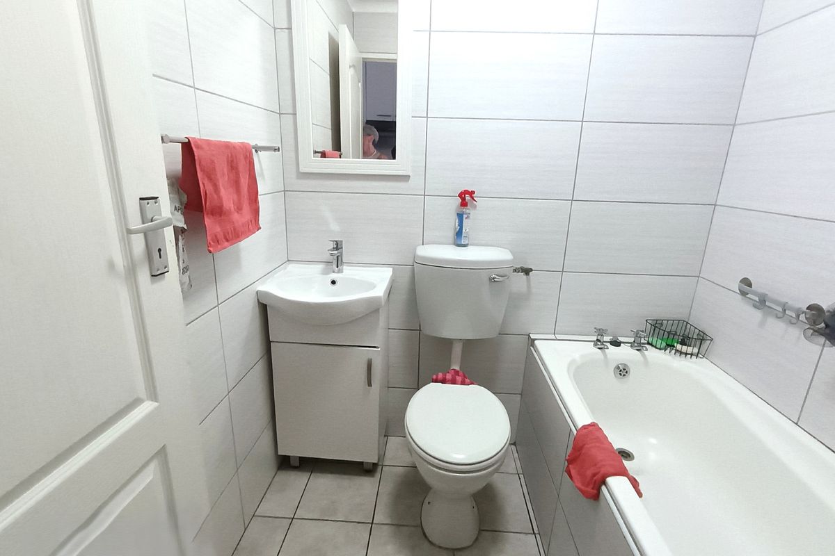 A compact bathroom featuring a white vanity, toilet, and bathtub with full-height wall tiling and neutral floor tiles.