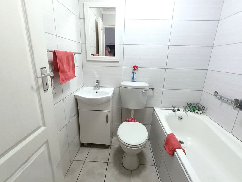A compact bathroom featuring a white vanity, toilet, and bathtub with full-height wall tiling and neutral floor tiles.
