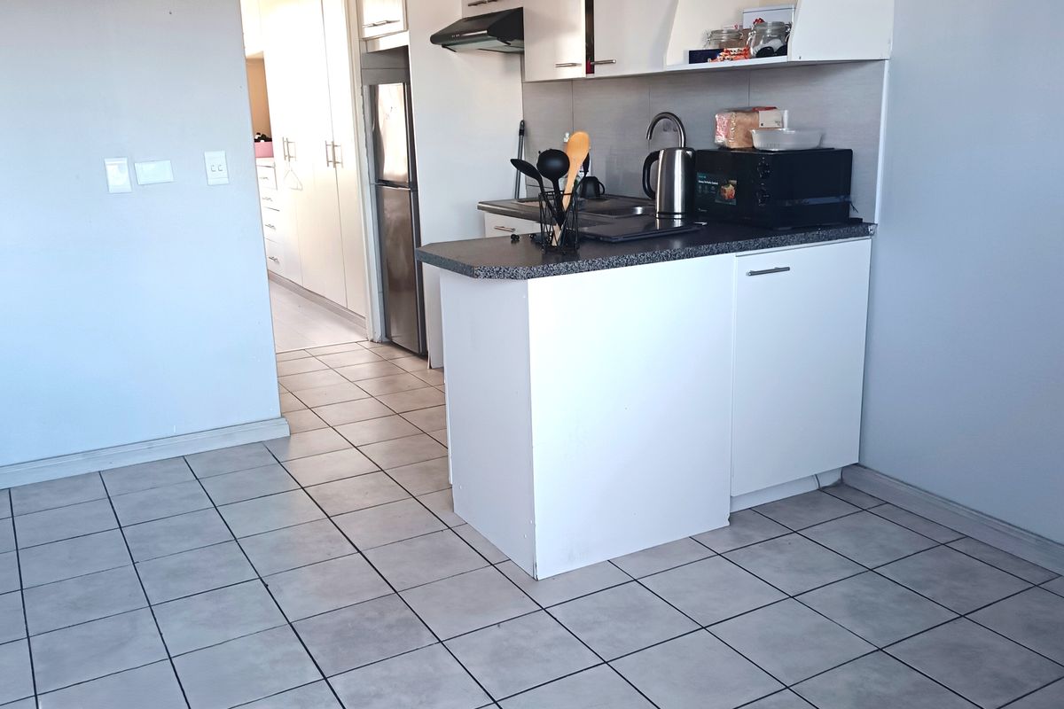 Compact kitchen featuring white built-in cabinetry, laminate countertops, a stainless steel sink, and an extractor fan, finished with neutral floor tiles.