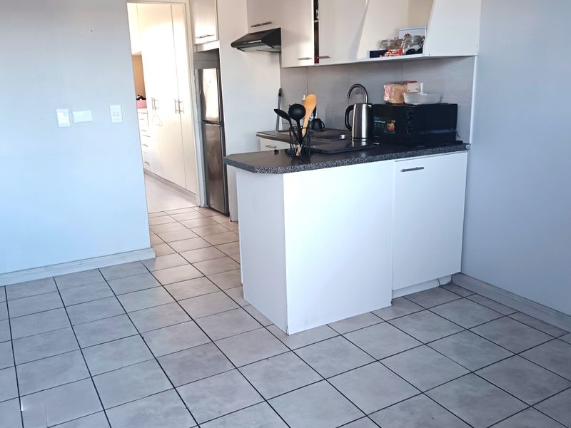 Compact kitchen featuring white built-in cabinetry, laminate countertops, a stainless steel sink, and an extractor fan, finished with neutral floor tiles.