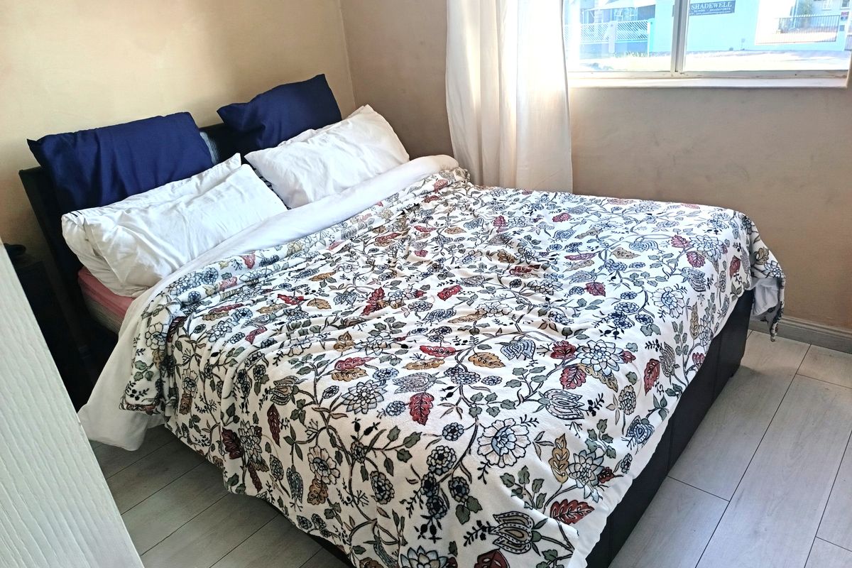 A bedroom featuring light-toned laminate flooring and a window providing natural light. The walls show signs of wear and require cosmetic attention.