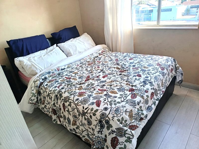 A bedroom featuring light-toned laminate flooring and a window providing natural light. The walls show signs of wear and require cosmetic attention.
