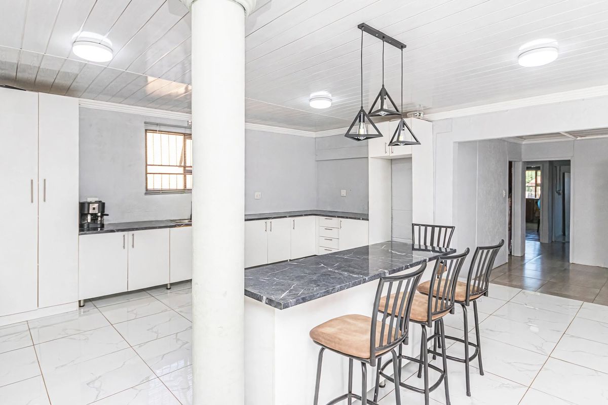 A bright, open-plan kitchen featuring white cabinetry, a marble-look breakfast bar, tiled flooring, and modern pendant lighting.