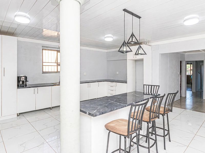 A bright, open-plan kitchen featuring white cabinetry, a marble-look breakfast bar, tiled flooring, and modern pendant lighting.
