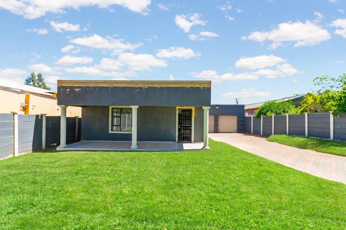 Rear view of the property featuring a covered patio with columns, a spacious lawn, paved driveway, and a detached double garage.