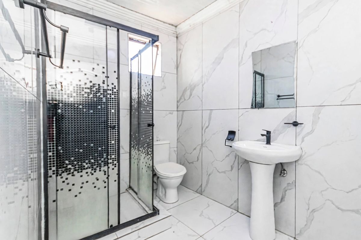 A modern bathroom featuring marble-look wall tiles, a pedestal basin, and a glass-enclosed shower unit.
