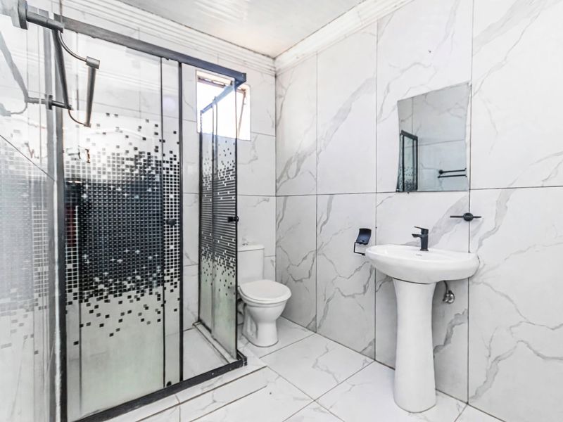 A modern bathroom featuring marble-look wall tiles, a pedestal basin, and a glass-enclosed shower unit.
