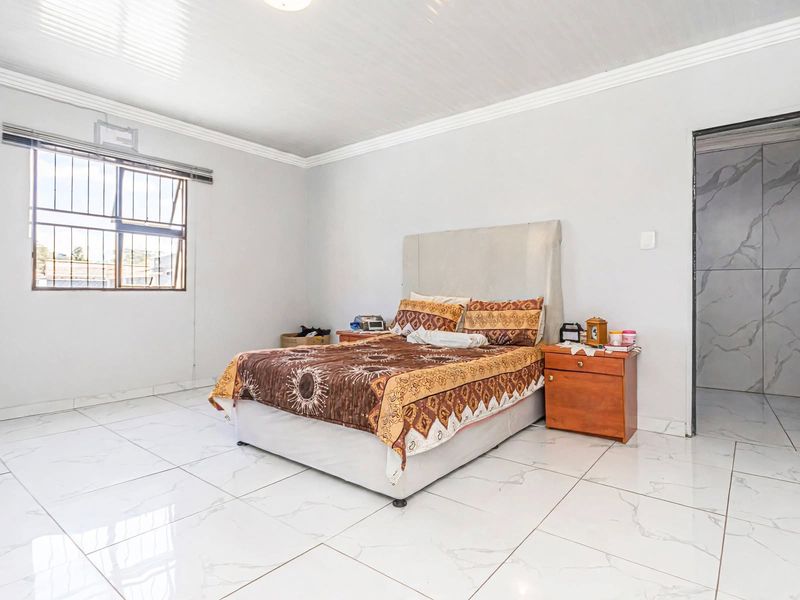 Spacious bedroom featuring modern white marble-look floor tiles, coved ceilings, and direct access to an en-suite bathroom.