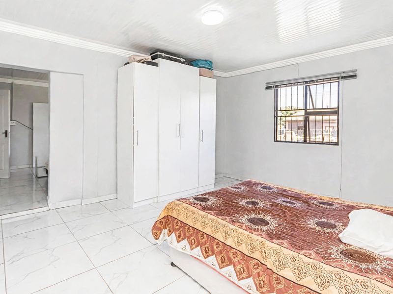 A bedroom featuring tiled flooring, a built-in wardrobe, and a window fitted with security bars.